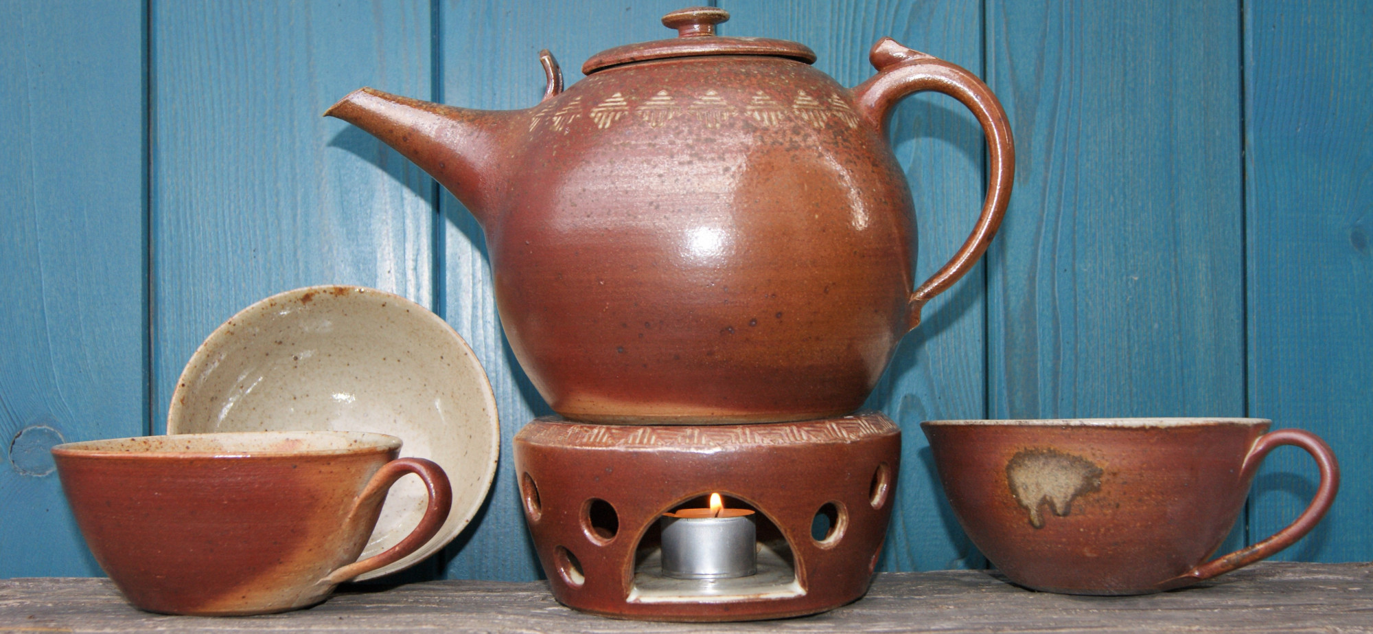 Teekanne mit Stövchen und drei Teetassen aus Holzbrandkeramik